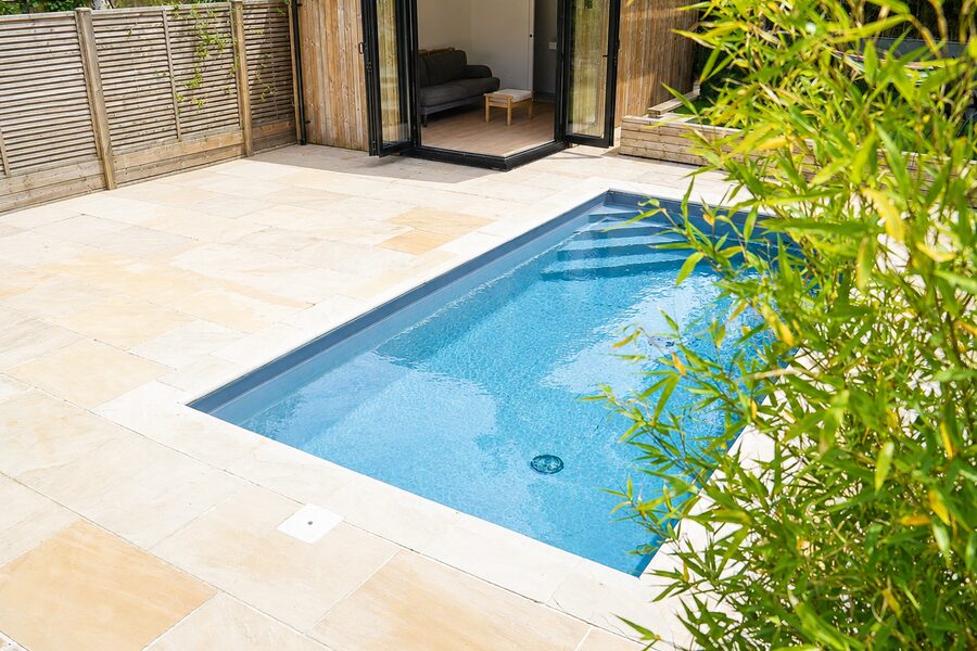 Compact spool with wide entry steps set into sandstone paving, beside a garden room with open bi-fold doors and bamboo planting