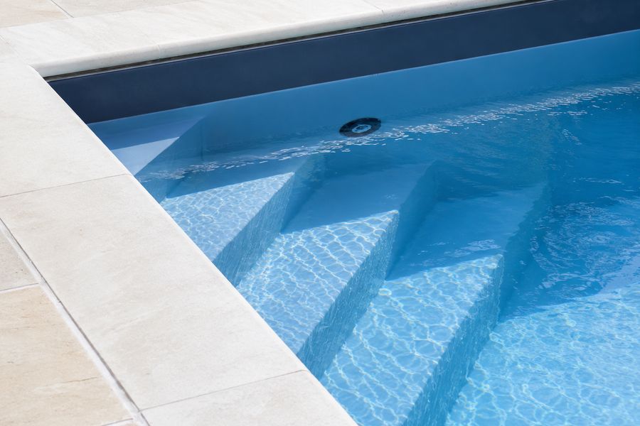 Wide entry steps in a garden pool with pale limestone coping and clear blue water