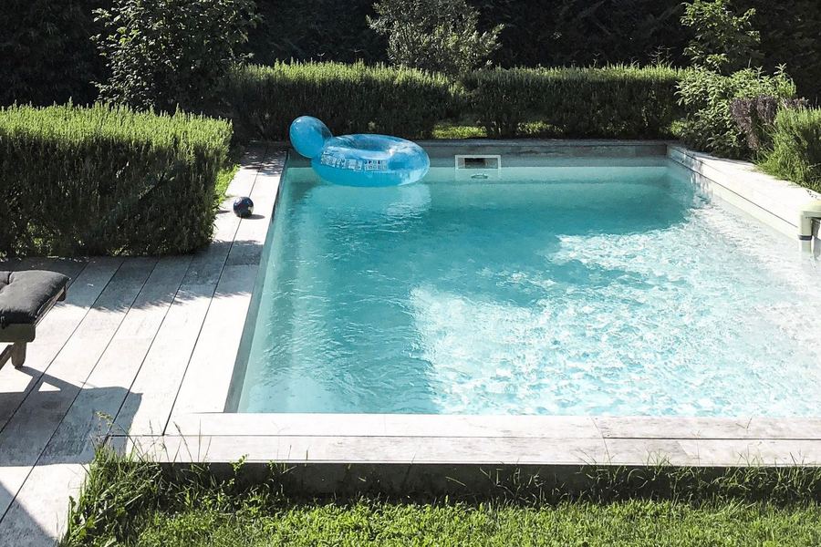 Full-size garden pool bordered by lawn, hedging and a lounger, set within an established garden