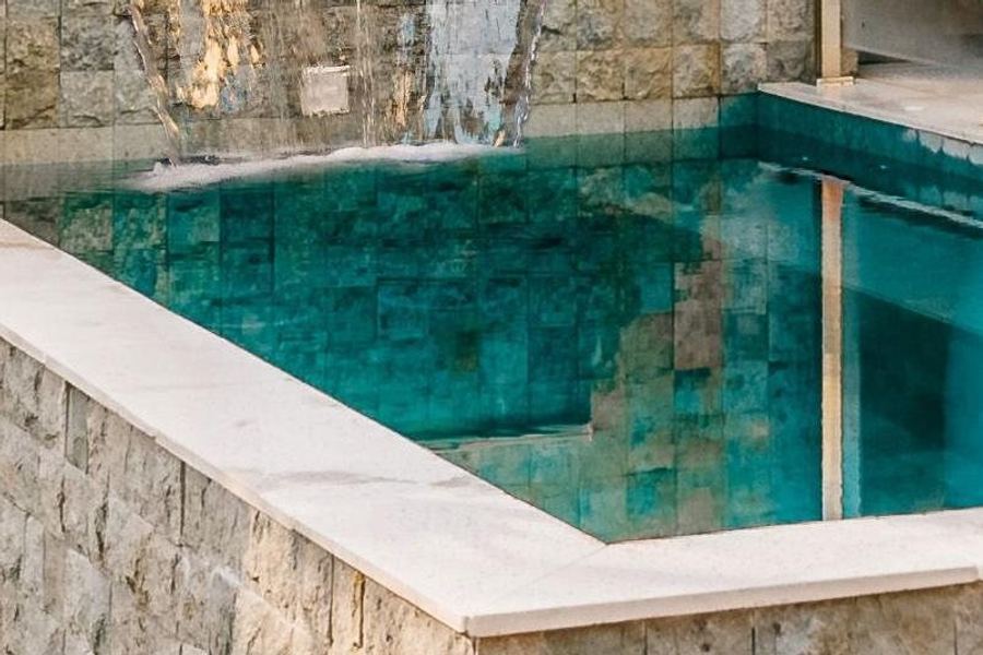 Compact raised plunge pool with tiled walls and a water feature, tucked into a small garden corner