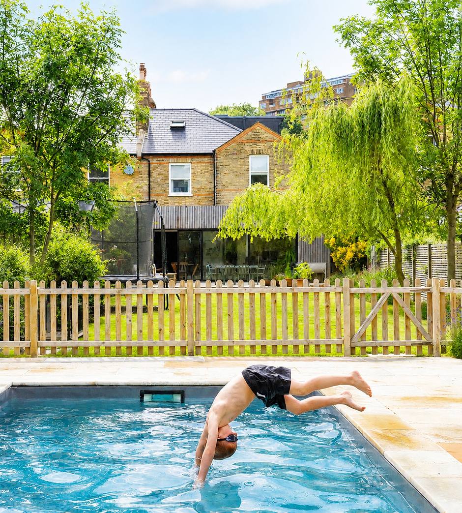 A child diving into a garden swimming pool, with lawn, picket fencing and a London townhouse behind